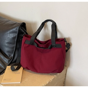 Detail view of burgundy canvas tote bag with adjustable black shoulder strap on display stand