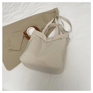 Vue à plat d'un sac cabas minimaliste en nylon beige avec large bandoulière sur fond blanc