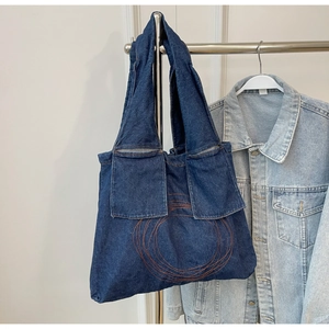Detailed macro of dark blue denim tote bag featuring dual front pockets and ring embroidery