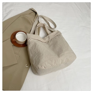 Détail d'un grand sac fourre-tout beige en nylon sur un lit avec des accessoires mode