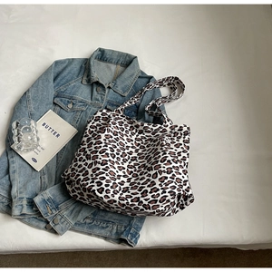 Flat lay view of a large leopard print tote bag with denim jacket on white background