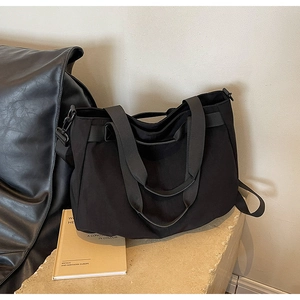 Detailed view of the black canvas tote bag with reinforced handles on a stone pedestal