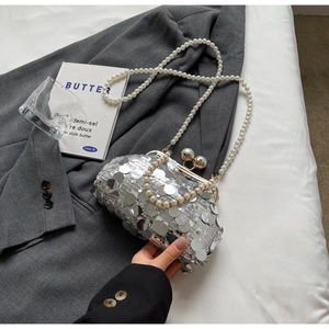 Detail of silver sequin evening bag with pearl strap on elegant suit and book