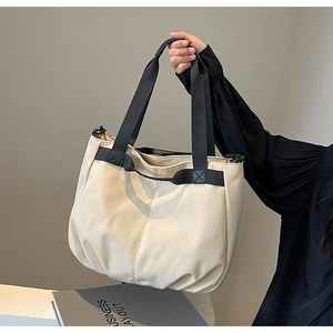 Close-up of a large beige canvas tote bag with black strap handles for women