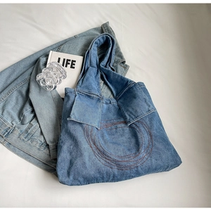 Detail of washed blue denim tote bag with red-brown embroidery and shirt-collar strap design
