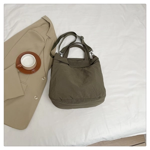 Gros plan du sac cabas en nylon vert olive avec bandoulière réglable sur tissu blanc