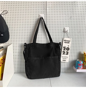 Dettaglio della borsa tote in denim nero con doppie tasche frontali e anelli in metallo