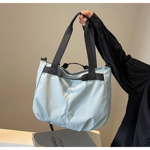 Detail of light blue nylon tote bag with black wide straps held by a model for daily commute