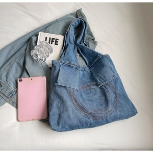 Detail showing blue denim tote bag with red circular embroidery on soft white bedding