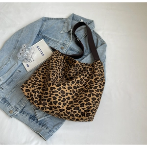 Flat lay of leopard print canvas tote bag with adjustable brown strap on white linen
