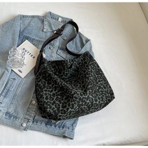 Flat lay of green leopard canvas tote bag with adjustable brown leather strap on denim