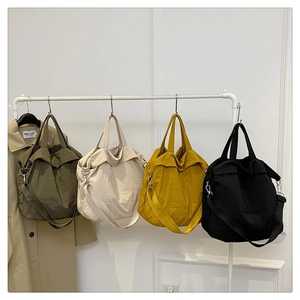 Détail de sacs cabas en nylon en olive, beige, jaune et noir suspendus au vestiaire