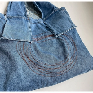 Detail view of blue washed denim tote bag featuring vintage brown circular stitching
