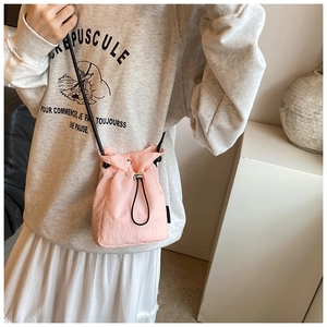 Pink drawstring bucket crossbody bag made of lightweight nylon fabric worn by a model