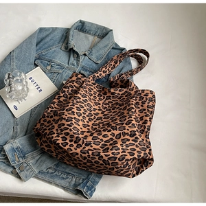 Close-up of leopard print tote bag placed on white bedding with fashion accessories