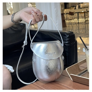 Macro detail of a silver metallic egg-shaped saddle bag with textured leather on a cafe table