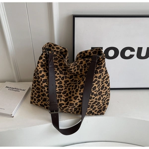 Detail of adjustable dark brown leather straps and metal buckle on leopard print canvas tote bag