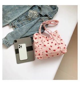 Detailed close-up of pink corduroy tote bag with red strawberry pattern on white desk
