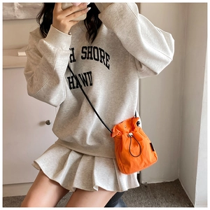 Detail of bright orange nylon drawstring bucket bag with black strap and metallic toggle