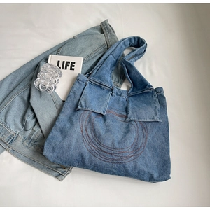 Detail of light blue denim tote bag featuring retro circular embroidery and front flap pockets