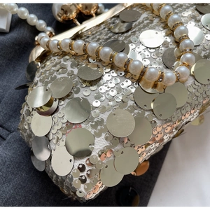 Detail of evening bag with gold sequins, large pearls handle, and metallic frame