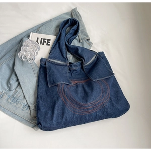 Detail of blue denim tote bag with orange stitching and unique collar-shaped handle design