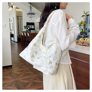 Gros plan sur un cabas en toile crème avec motif floral vert et nœud en dentelle