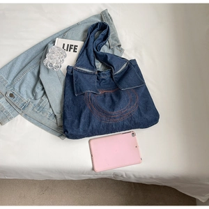 Detail of blue denim tote bag featuring orange circular embroidery and ample interior space