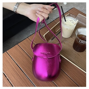 Metallic magenta leather saddle bag on wooden table with coffee detail view