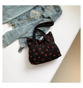 Detail of black corduroy tote bag featuring red strawberry embroidery and dual handles