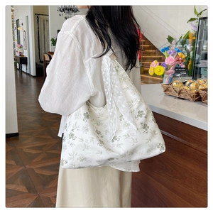 Détail d'un sac cabas floral en toile avec nœud en dentelle porté par un mannequin