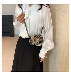 Detail of trendy leopard print crossbody bag with silver buckle worn on white satin shirt