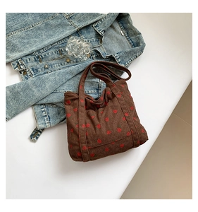 Detail shot of brown corduroy tote bag with red strawberry embroidery on denim jacket