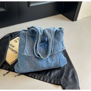 Detail of light blue denim tote bag featuring red circular embroidery and sturdy handles
