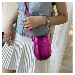 Detail of a bright magenta saddle bag with metallic finish and delicate shoulder strap