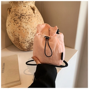 Detail of light pink drawstring mini bucket bag with textured nylon fabric and black cord