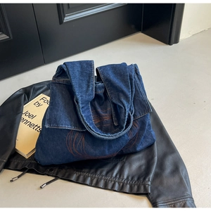 Detail of blue denim tote bag with orange circular stitching on black leather jacket