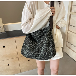 Detail of green leopard canvas tote bag with wide brown leather strap on model