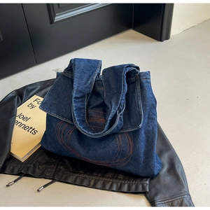 Close-up of dark blue denim tote bag with orange circular embroidery and wide strap