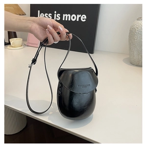 Detailed close-up of small black shiny leather saddle bag with fashion brand engraving