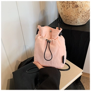 Detail of light pink nylon bucket bag with drawstring closure and slim black strap