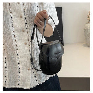 Detail of a minimalist black PU leather saddle bag with button closure and embossed text