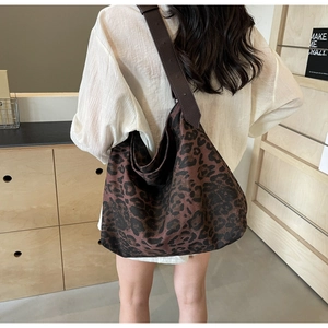 Leopard print canvas tote bag with brown leather strap worn by model in a cozy setting
