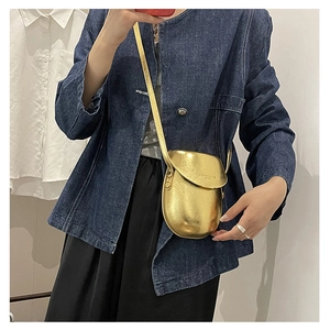 Model wearing a gold metallic pebble shaped crossbody phone bag with reflective mirror finish