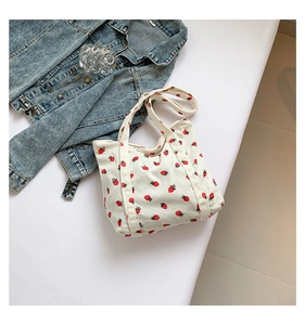 Detailed texture of white corduroy tote bag with red strawberry pattern on a table
