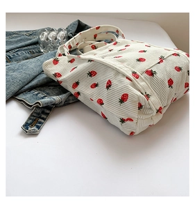 Detail of white corduroy tote bag with red strawberry print and long shoulder strap