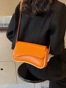Retro oranje schoudertas met witte golvende bies gedragen door model in zwarte getextureerde blazer