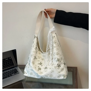 Détail du sac cabas en toile florale avec motifs végétaux verts et nœud en dentelle blanche