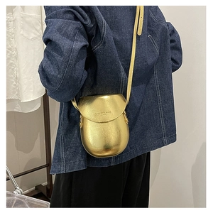 Detail view of metallic gold saddle bag with smooth liquid finish and long strap on model