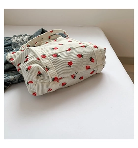 Detail of cream corduroy tote bag showing red strawberry embroidery and ribbed texture